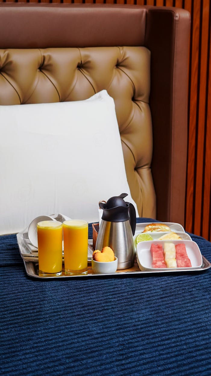 Cozy hotel room breakfast with juice, fruit, and coffee on tray.